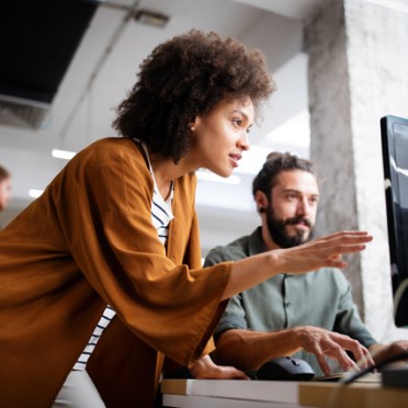 Donna con capelli ricci che gesticola mentre collabora con collega su computer portatile in ufficio